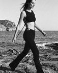 Woman walking on rocks by the sea wearing a black outfit.