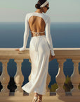 Woman in a white dress standing on a balcony overlooking the ocean.