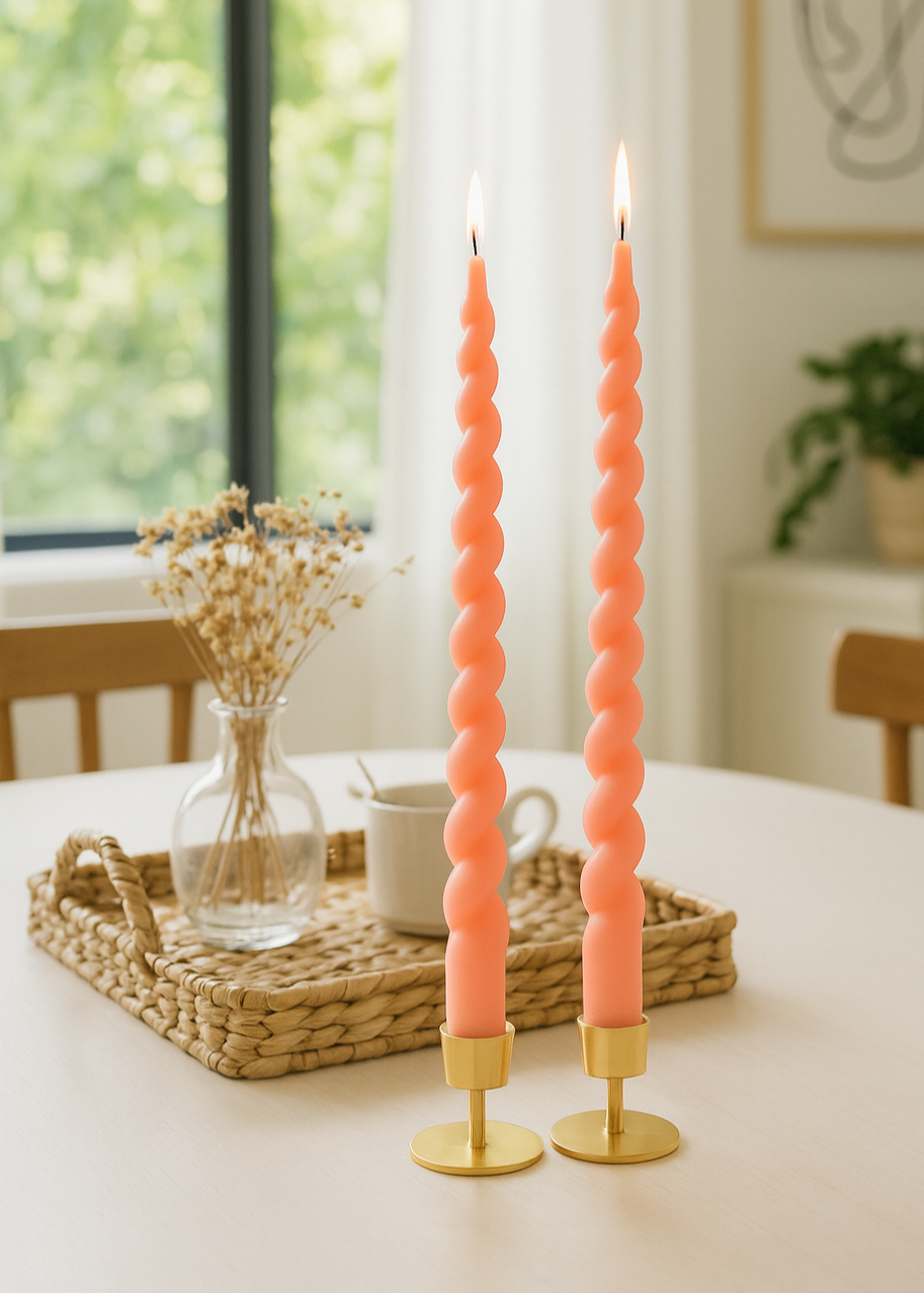 Two spiral pink candles on gold stands on a table with a blurred background